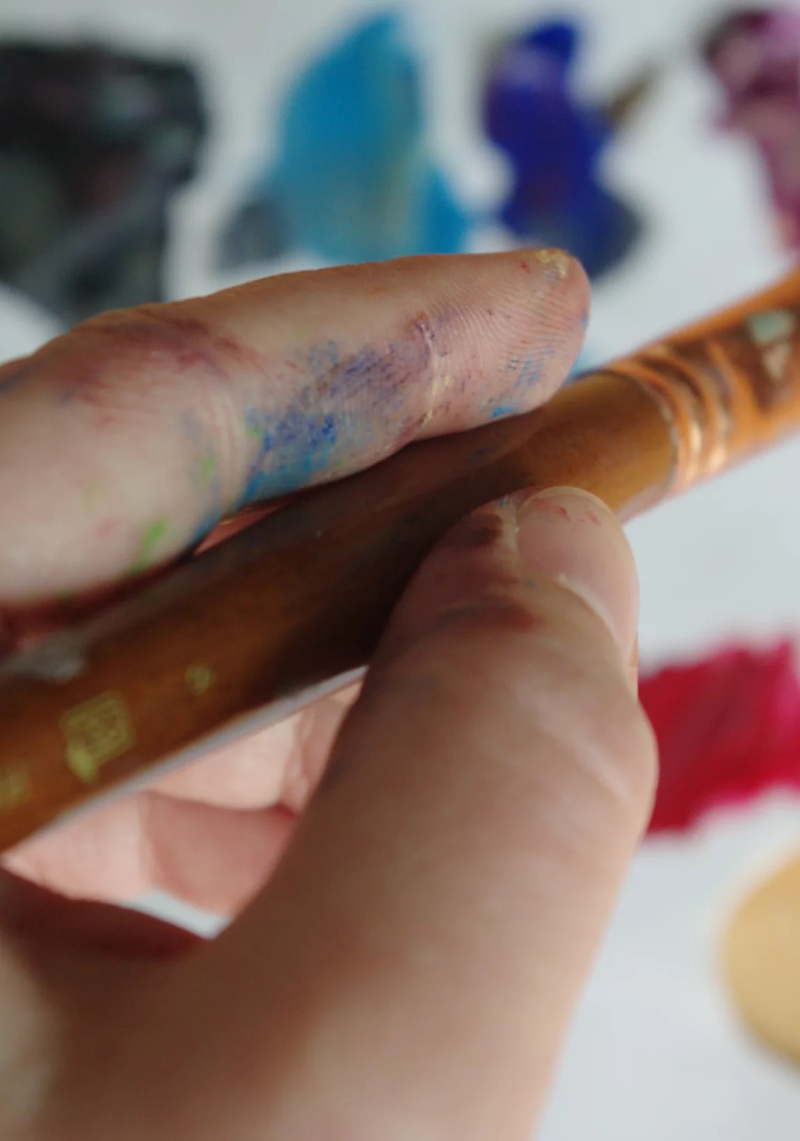 Hand
        covered in paint, holding a paintbrush.